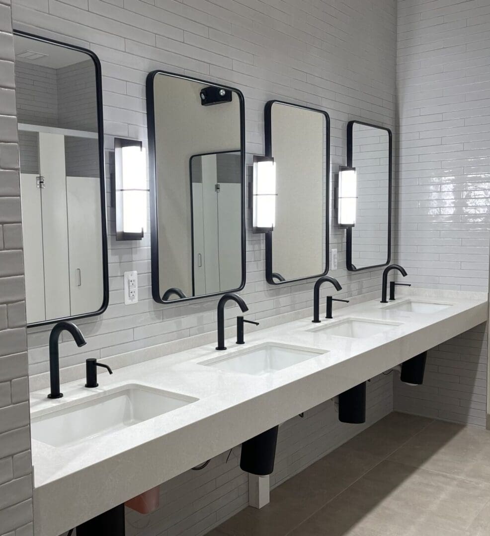 A bathroom with four sinks and mirrors in it.