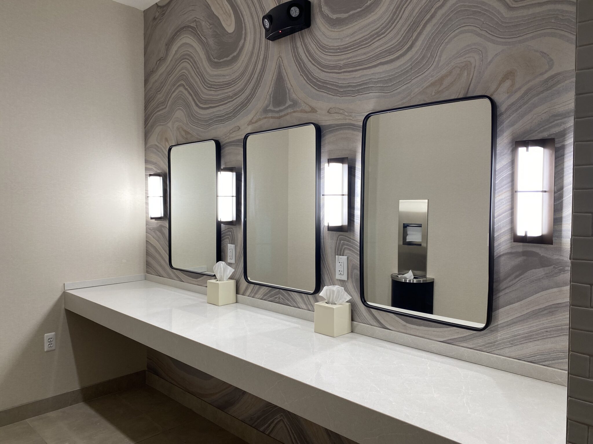 A bathroom with three mirrors and two soap dispensers.