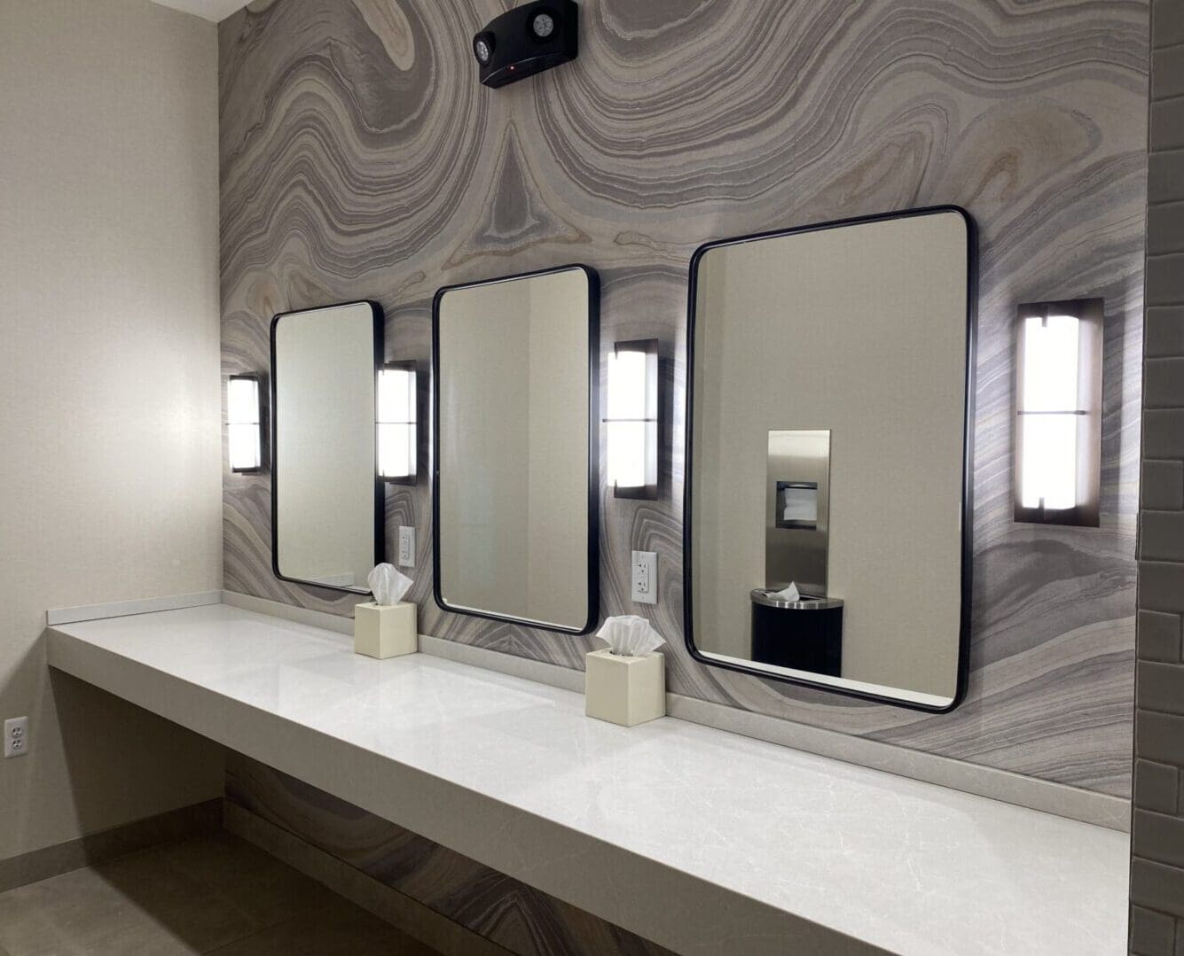 A bathroom with three mirrors and two soap dispensers.