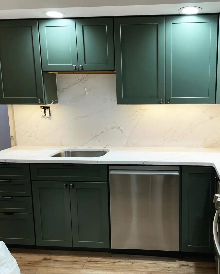 A kitchen with green cabinets and white countertops.