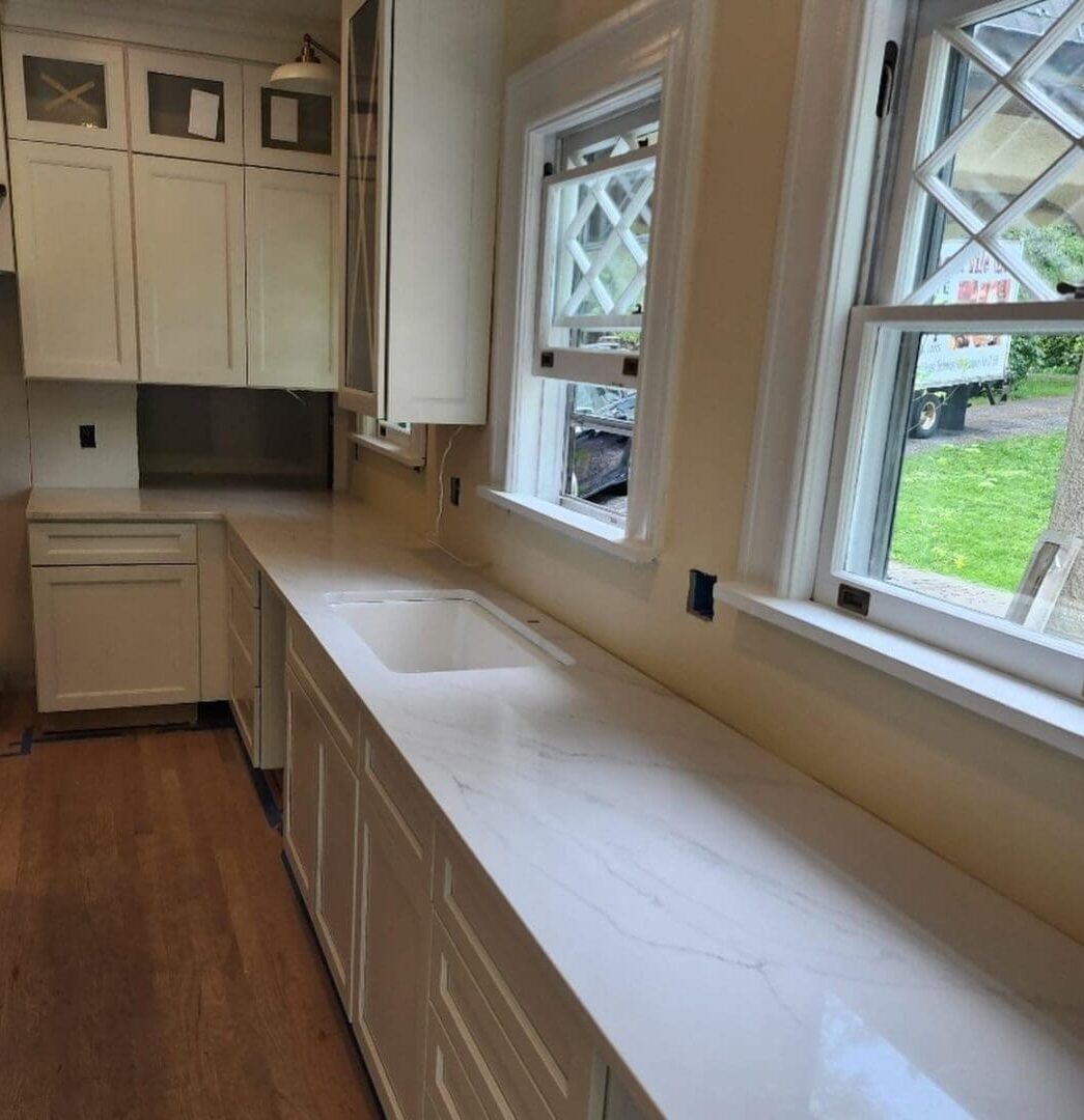 White kitchen countertop with sink and windows.