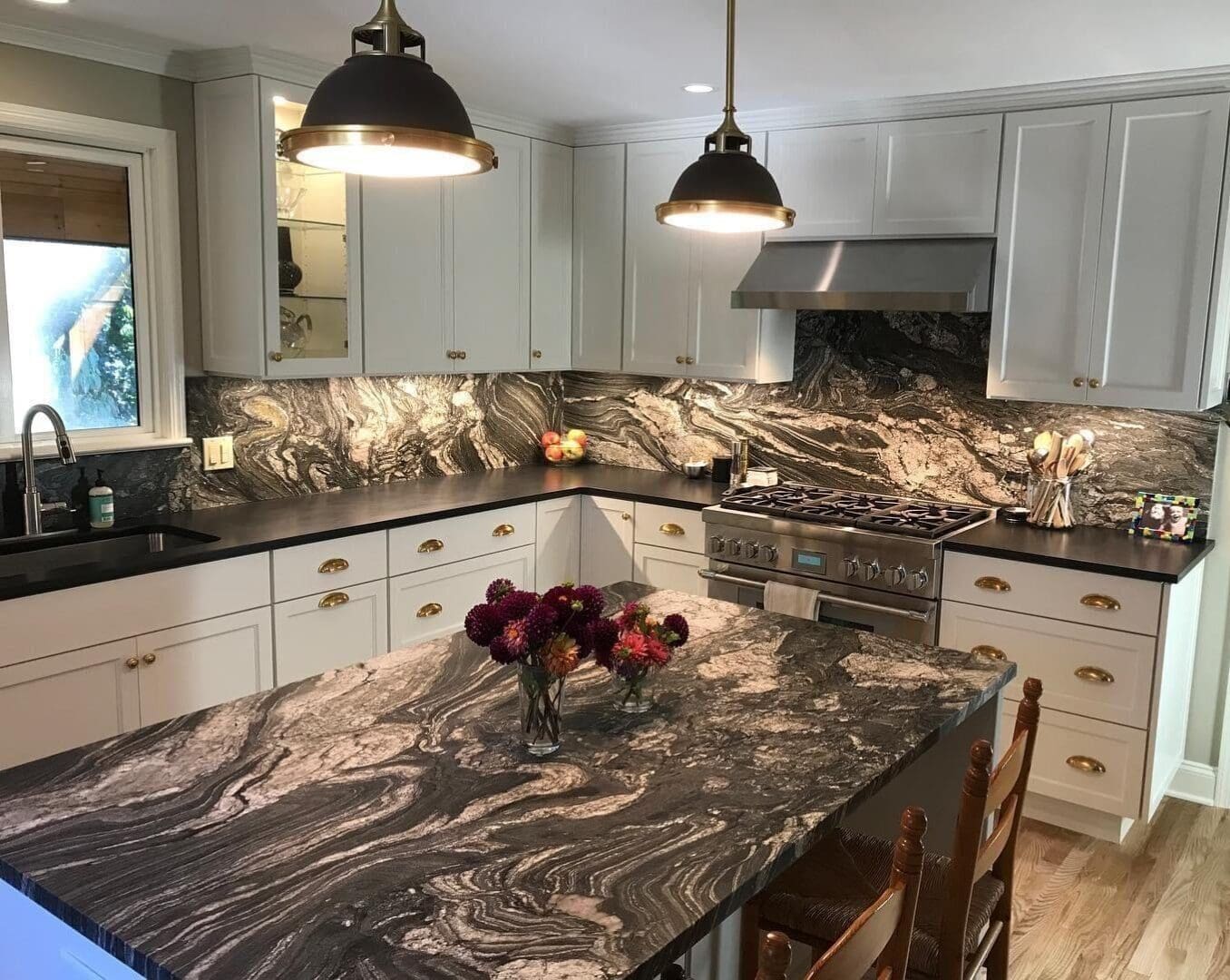 A kitchen with marble counter tops and white cabinets.