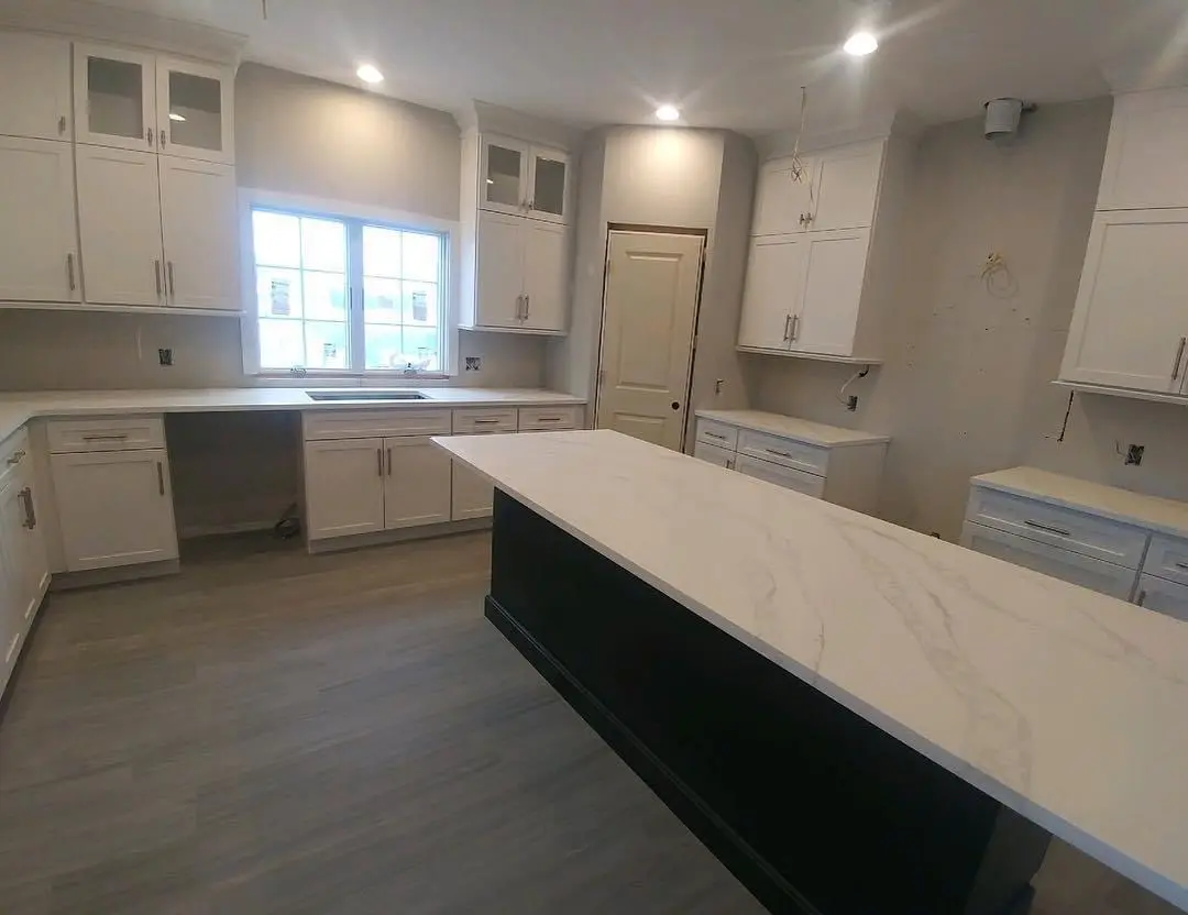 A kitchen with white cabinets and black island.