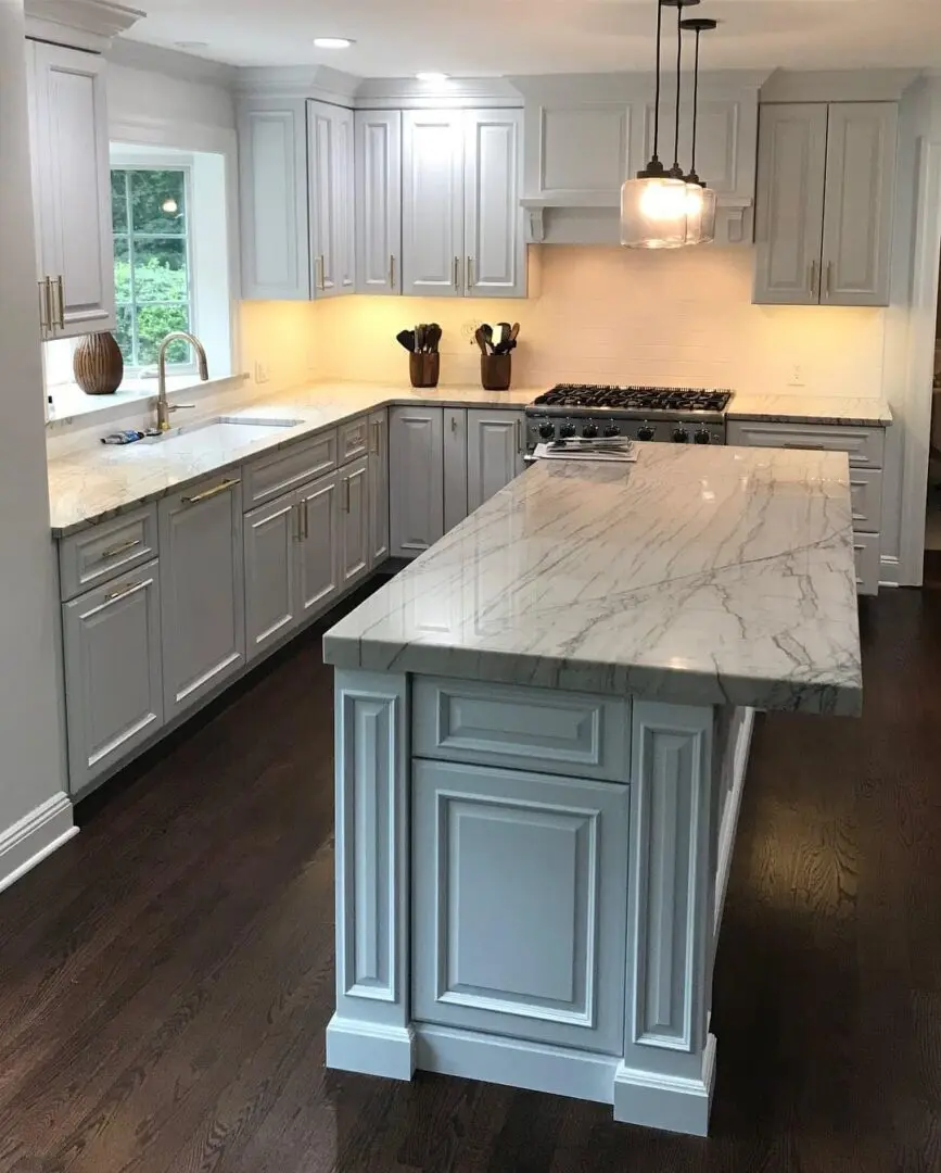 A kitchen with white cabinets and marble counter tops.