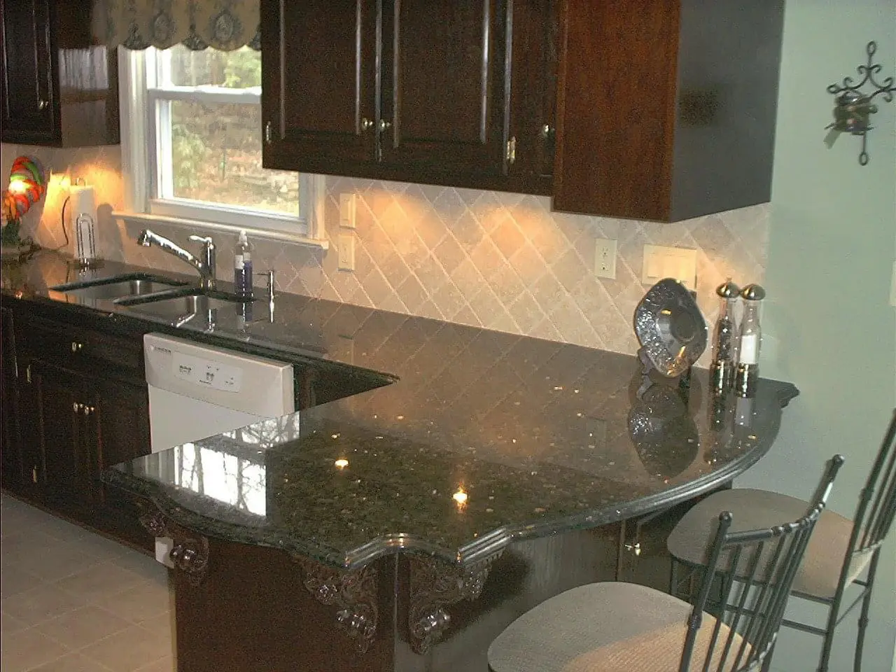 A kitchen with granite counter tops and dark wood cabinets.