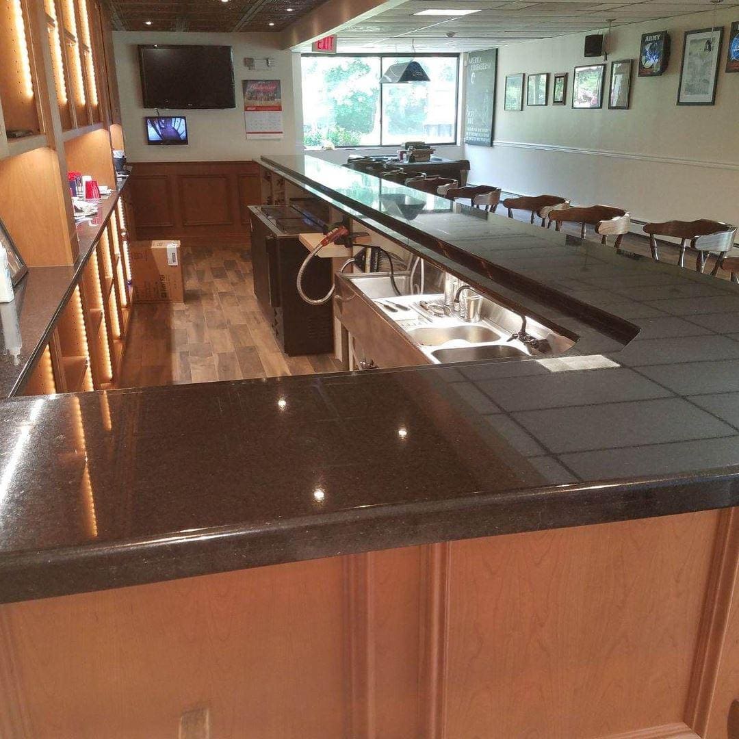 A bar with black counter tops and wooden cabinets.