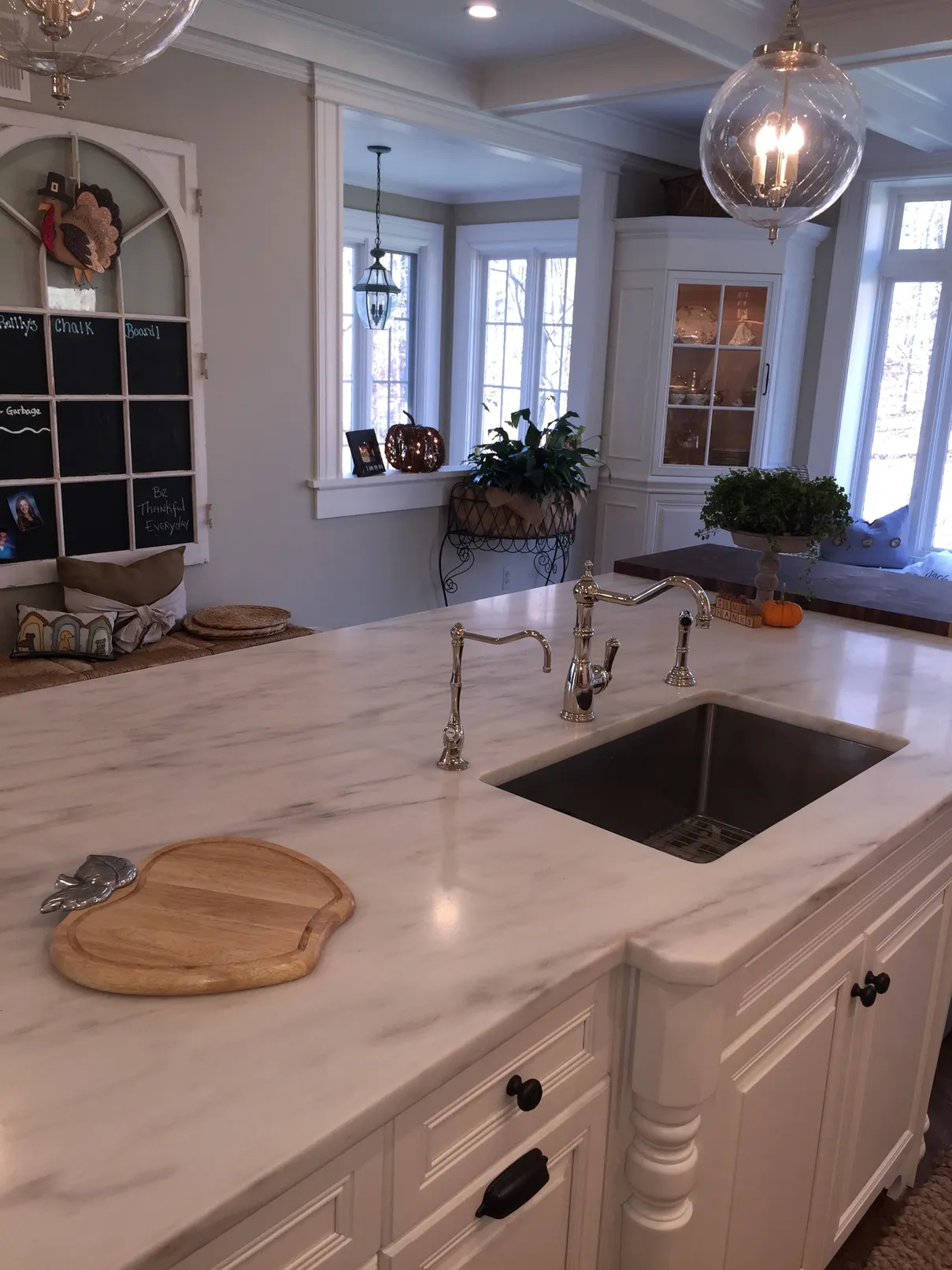 White kitchen island with sink and cutting board.