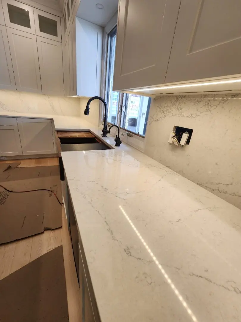 A kitchen with marble counter tops and white cabinets.