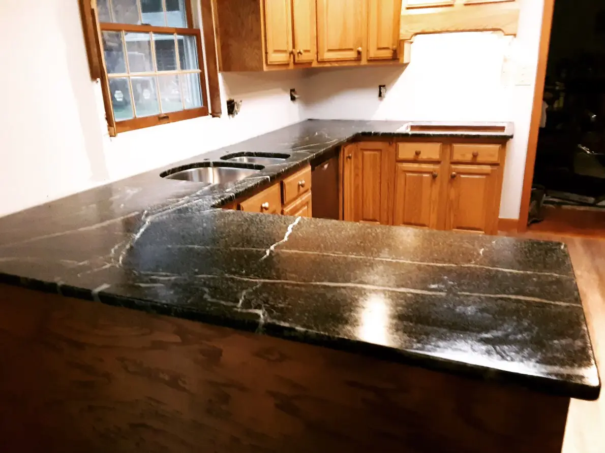 A kitchen with black marble counter tops and wooden cabinets.