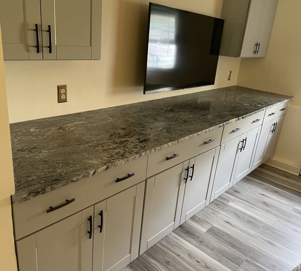 Granite countertop with gray cabinets and TV.